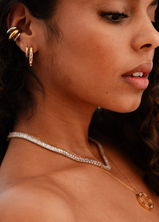 Close-up of a woman wearing gold earrings and a necklace with a dark background