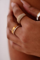 Close-up of a hand wearing multiple diamond-studded rings on a neutral background