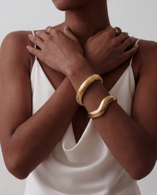 Person wearing a gold bracelet on a plain background