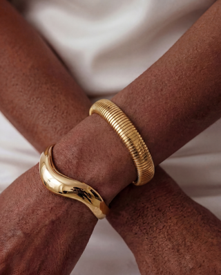 Gold bangles on a person's wrist against a neutral background