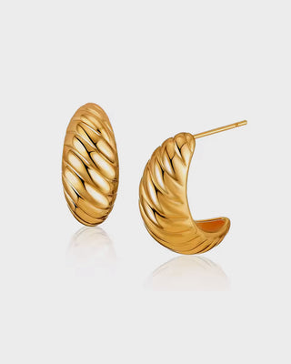 "Close-up of Queen & Collection's Pera Earrings, featuring sculpted high-polish 18K gold-plated hoops with a bold, curved silhouette."


