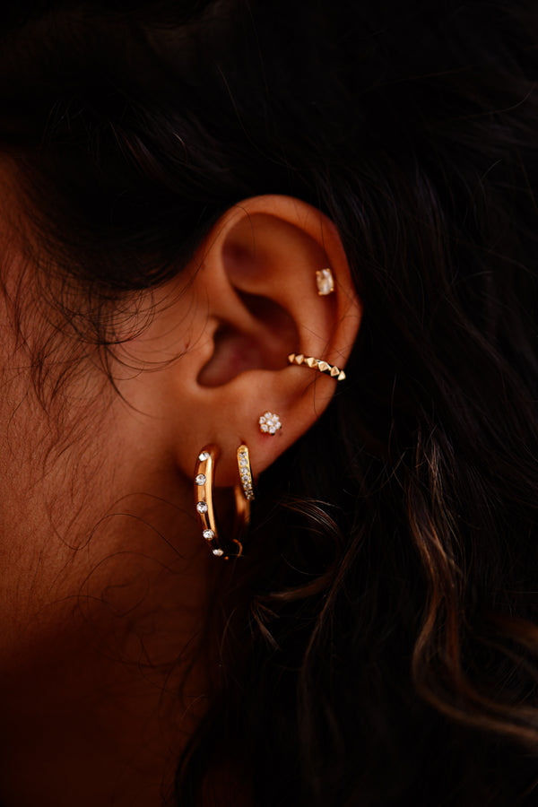 Close-up of an ear wearing gold hoop earrings with a dark background