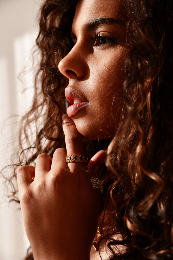 Close-up of a woman with curly hair and a hand resting on her chin, wearing a gold ring.