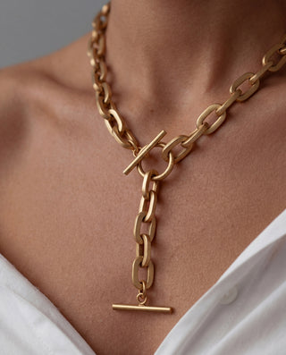Gold chain necklace with a clasp on a person wearing a white top.