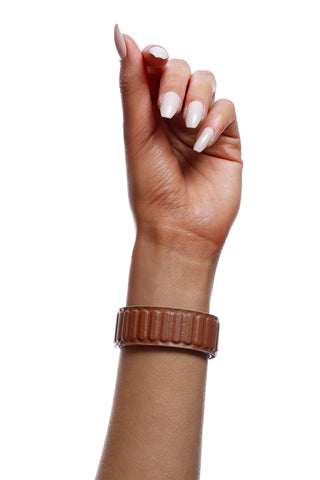 Hand wearing a brown ribbed bracelet on a white background