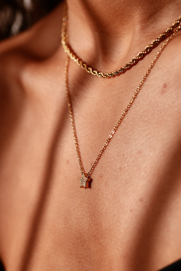 Close-up of a person wearing a rose gold necklace with a small pendant on a blurred background