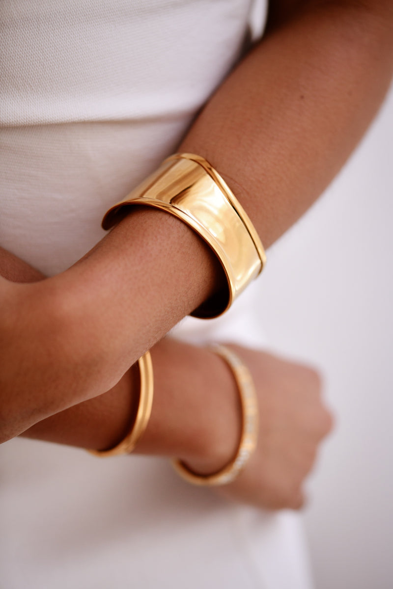 Gold bangles on a person's wrist against a white background