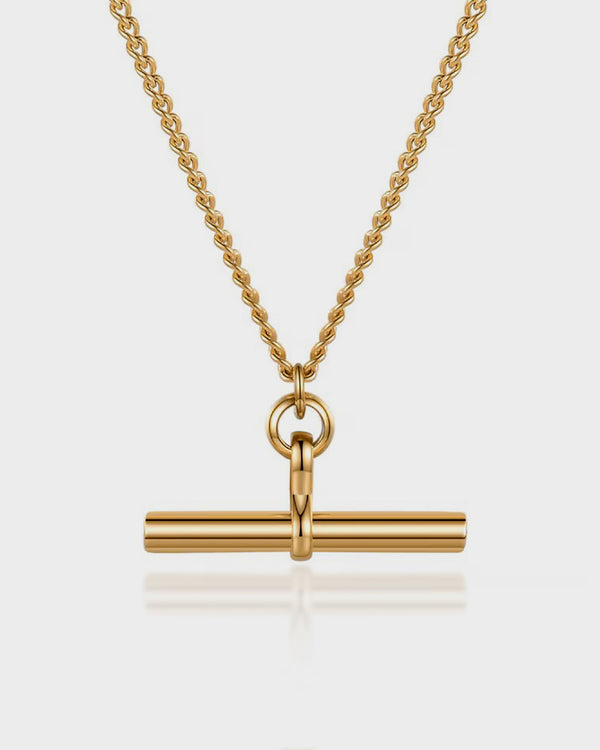 Gold necklace with a cylindrical pendant on a light gray background