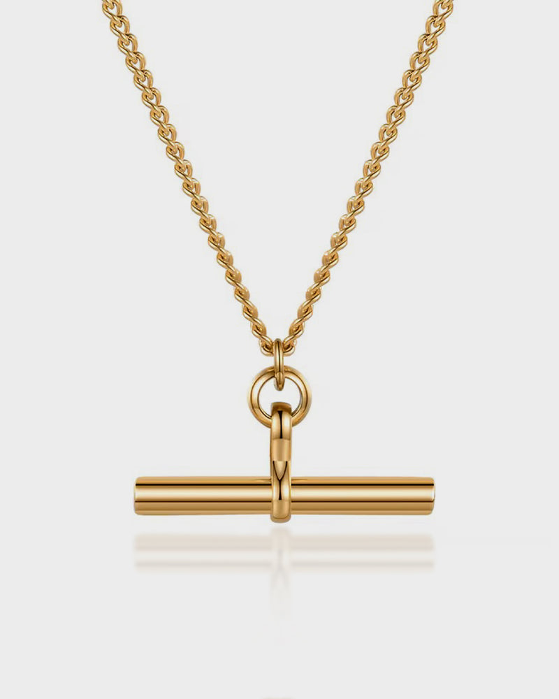 Gold necklace with a cylindrical pendant on a light gray background