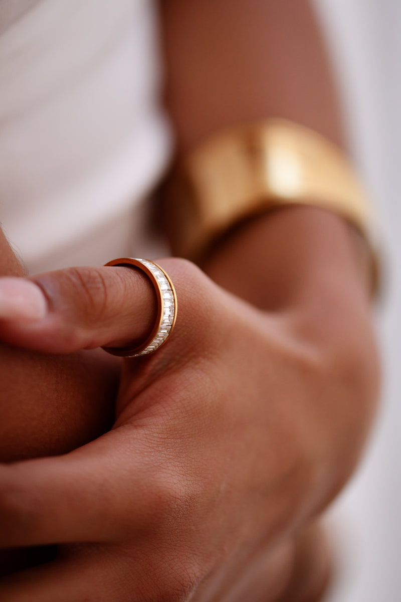 Close-up of a hand wearing a gold ring and bracelet on a blurred background
