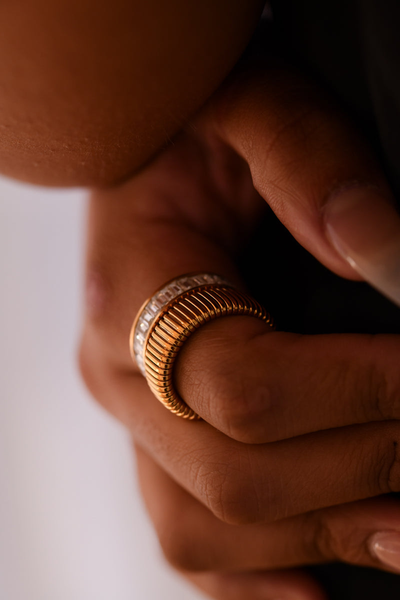Close-up of a hand wearing a gold ring with a textured band on a neutral background