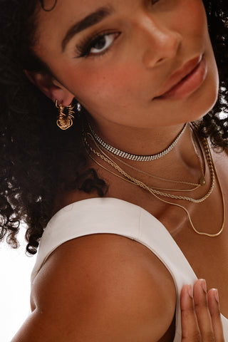 Close-up of a woman wearing gold earrings and necklaces with a white top.