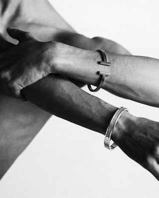 Two arms with bracelets on a plain background