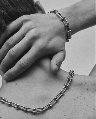 Person wearing a chain necklace and bracelet on a plain background