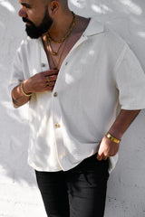 Man wearing a textured white shirt and black pants against a white wall