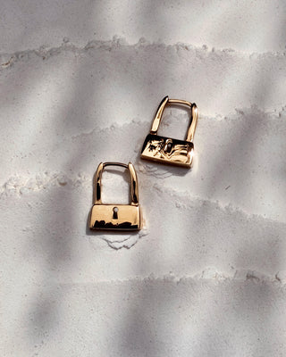 Gold padlock-shaped earrings on a textured gray surface