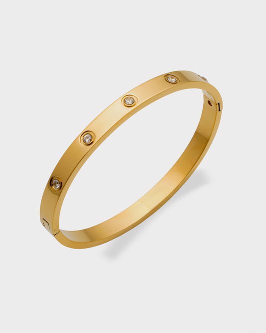 The Magnum Bracelet from Queen and Co. is a versatile, stackable piece crafted with 18K gold plating and zirconia accents. It is hypoallergenic, tarnish, and water-resistant, making it suitable for everyday wear. The bracelet combines affordability with luxury, offering a stylish accessory that complements various outfits.